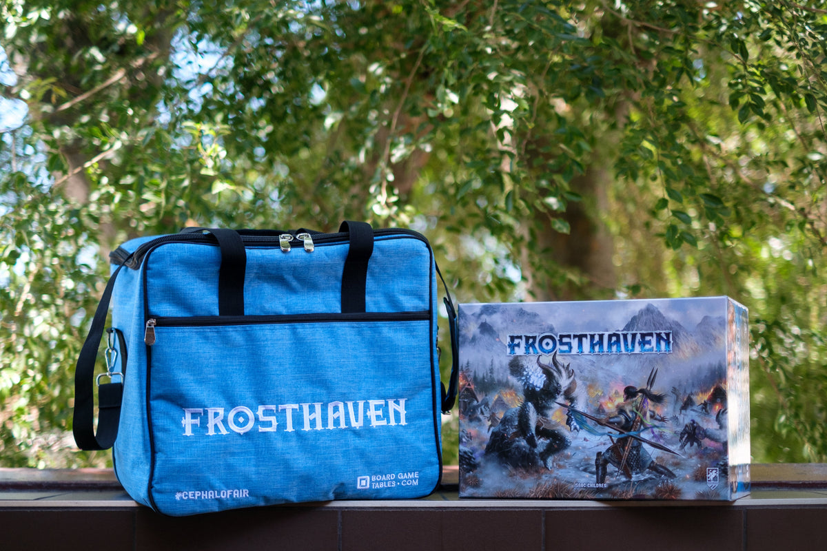 A blue premium game bag with the text 'FROSTHAVEN' on it, placed next to its packaging box with the game's name and an illustration of a frozen landscape.