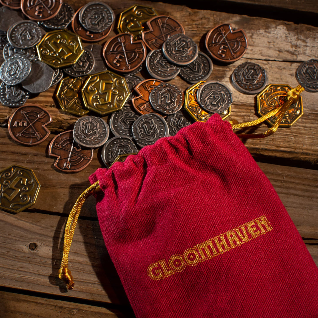 Red bag with 'Gloomhaven' branding on a wooden surface with coins.
